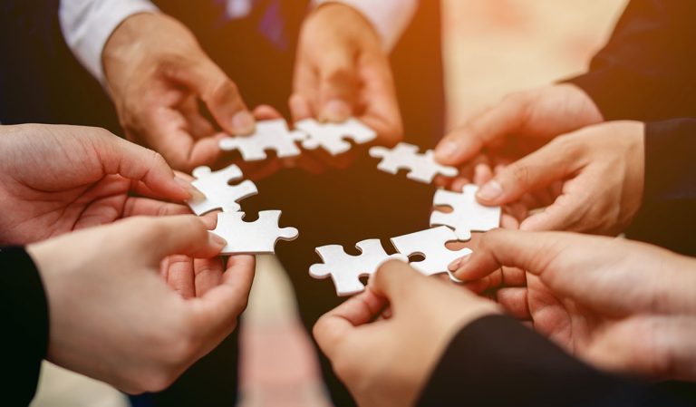 A group of hands holding puzzle pieces in a circle.