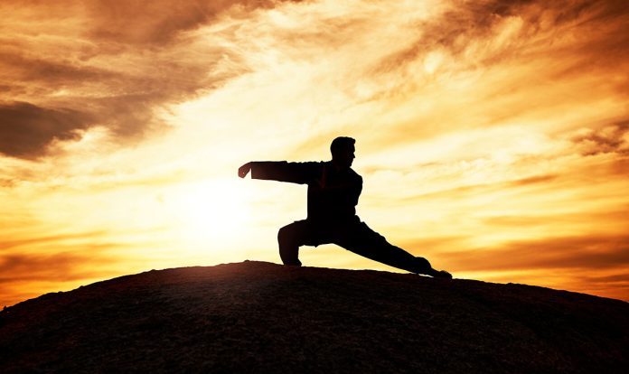 A man practicing martial arts forms on a hill at sunset.